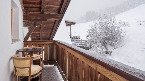 A wooden balcony with a chair, a table, and a snowy landscape view.