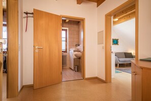 Un couloir avec une porte en bois donnant sur une salle de bain, un radiateur et, au fond, un canapé gris.