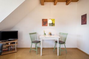 Una habitación con televisión sobre un mueble bajo, dos sillas, una mesita con lámpara y obras de arte en las paredes.