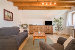Un salon avec un plafond en bois, un téléviseur, un meuble et une plante.