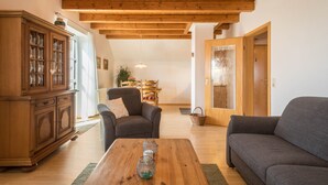 Ein Wohnzimmer mit Holzbalkendecke, einer Couch, einem Schrank und einem Essbereich im Hintergrund.