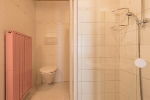 Un baño con inodoro, ducha y radiador rosa.