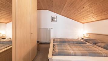 A bedroom with wooden ceiling, two beds with plaid bedding, a radiator, and a framed picture on the wall.