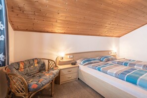 Un dormitorio con techo de madera, un sofá, una cama con ropa de cama a rayas y lámparas de noche.