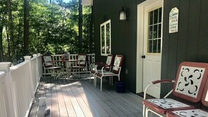 Una terraza de madera con barandas blancas, varias sillas y una puerta con un letrero.