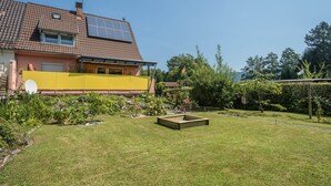 Una casa con panel solar, un muro amarillo y un jardín con maceta de madera.