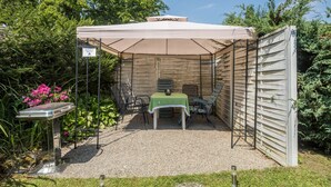 Un área de patio techada con una mesa y sillas, rodeada por una cerca de madera y follaje.
