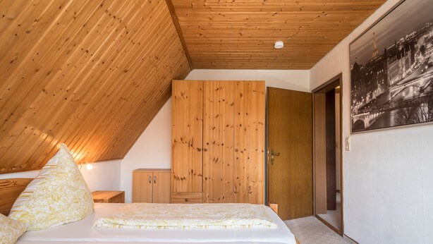 Un dormitorio con techo inclinado, armario de madera y cama con ropa de cama estampada.