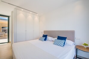Quarto com cama, almofadas, mesa de cabeceira e vista para área externa.