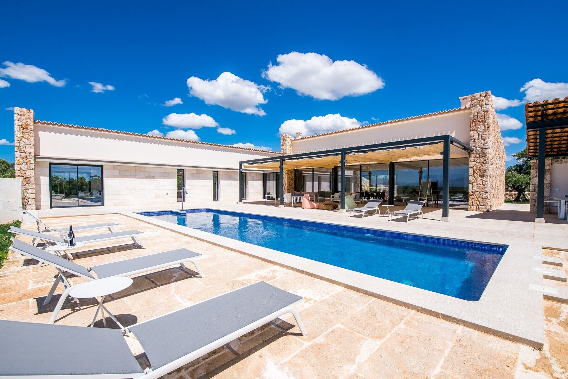 A modern pool area with lounge chairs, a covered seating area, and stone pillars.
