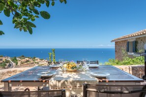 Une table dressée pour le dîner, avec vue sur la mer, un bâtiment en pierre et un ciel dégagé.