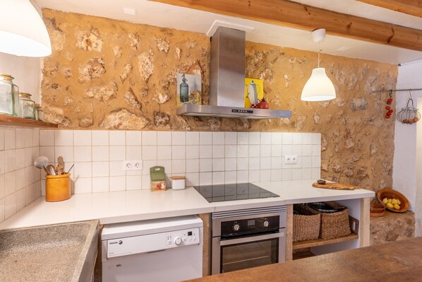 Une cuisine avec un mur en pierre, des carreaux blancs, une hotte de cuisine en acier inoxydable, un lave-vaisselle, un four et un luminaire suspendu.