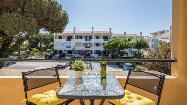 A balcony with a table, chairs, a potted plant, and a bottle. - Beautiful Marjoh AL Holiday Apartment with Pool, Balcony, Air Conditioning and Wi-Fi (Vilamoura, Quarteira)