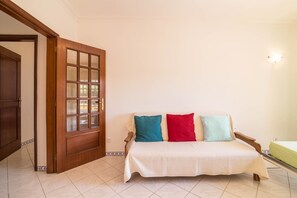 A room with a wooden door, a sofa with a white cover, and a bed with a green mattress. - Beautiful holiday apartment Marjoh AL with pool, balcony, air conditioning and Wi-Fi (Vilamoura, Quarteira)