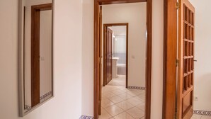 A corridor with wooden doors and tiled flooring leading to a bathroom. - Beautiful Marjoh AL Holiday Apartment with Pool, Balcony, Air Conditioning and Wi-Fi (Vilamoura, Quarteira)