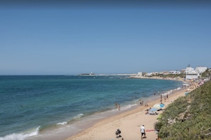 A coastal beach scene with a sandy shore, clear blue sea, and buildings in the background. - “Casa Vacacional en Caños de Meca” with Shared Pool (Caños de Meca)