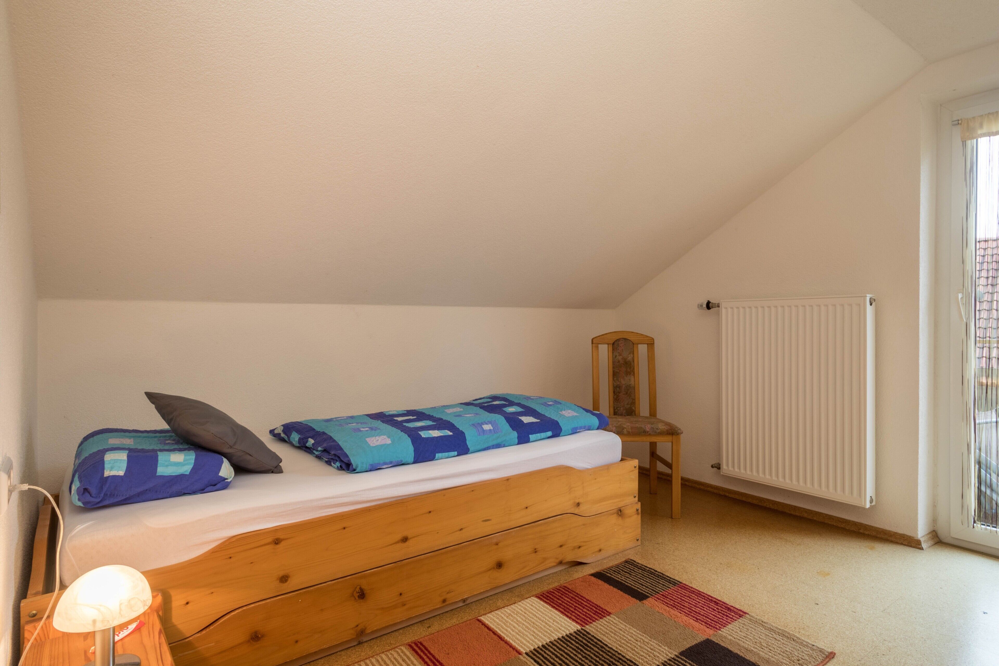 Et soveværelse med en enkelt seng, en radiator, en stol og en lampe.