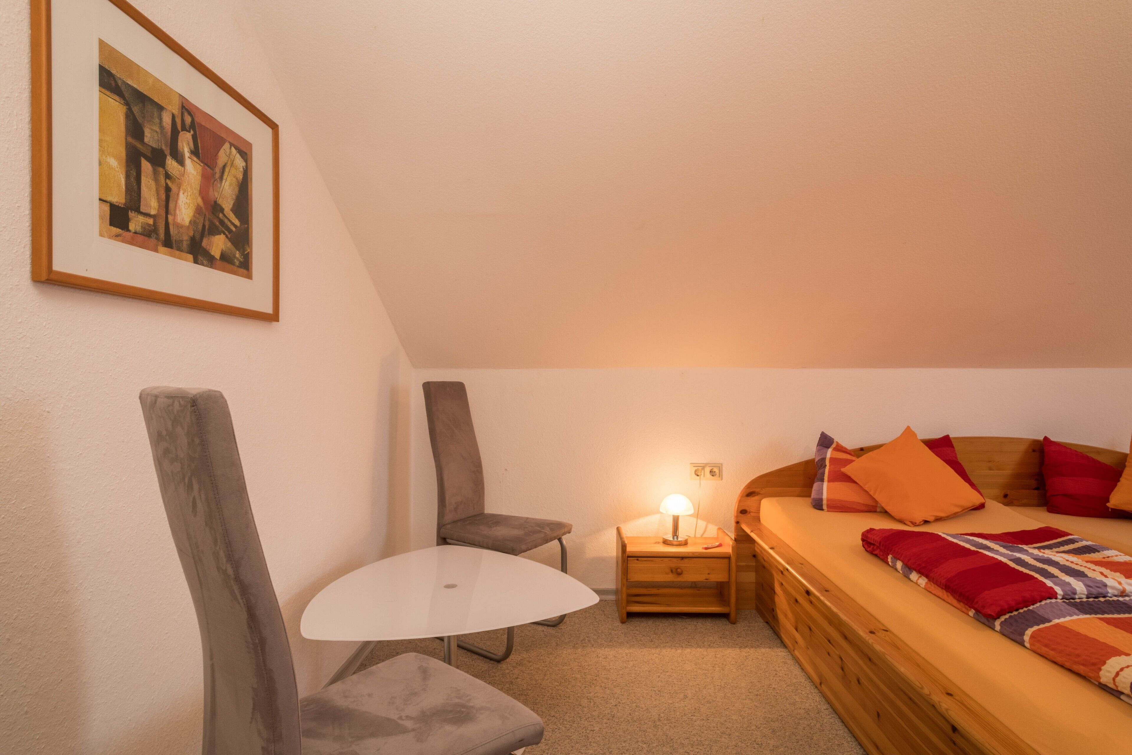 Une pièce confortable avec un lit, une petite table, une chaise et une table de chevet avec une lampe.