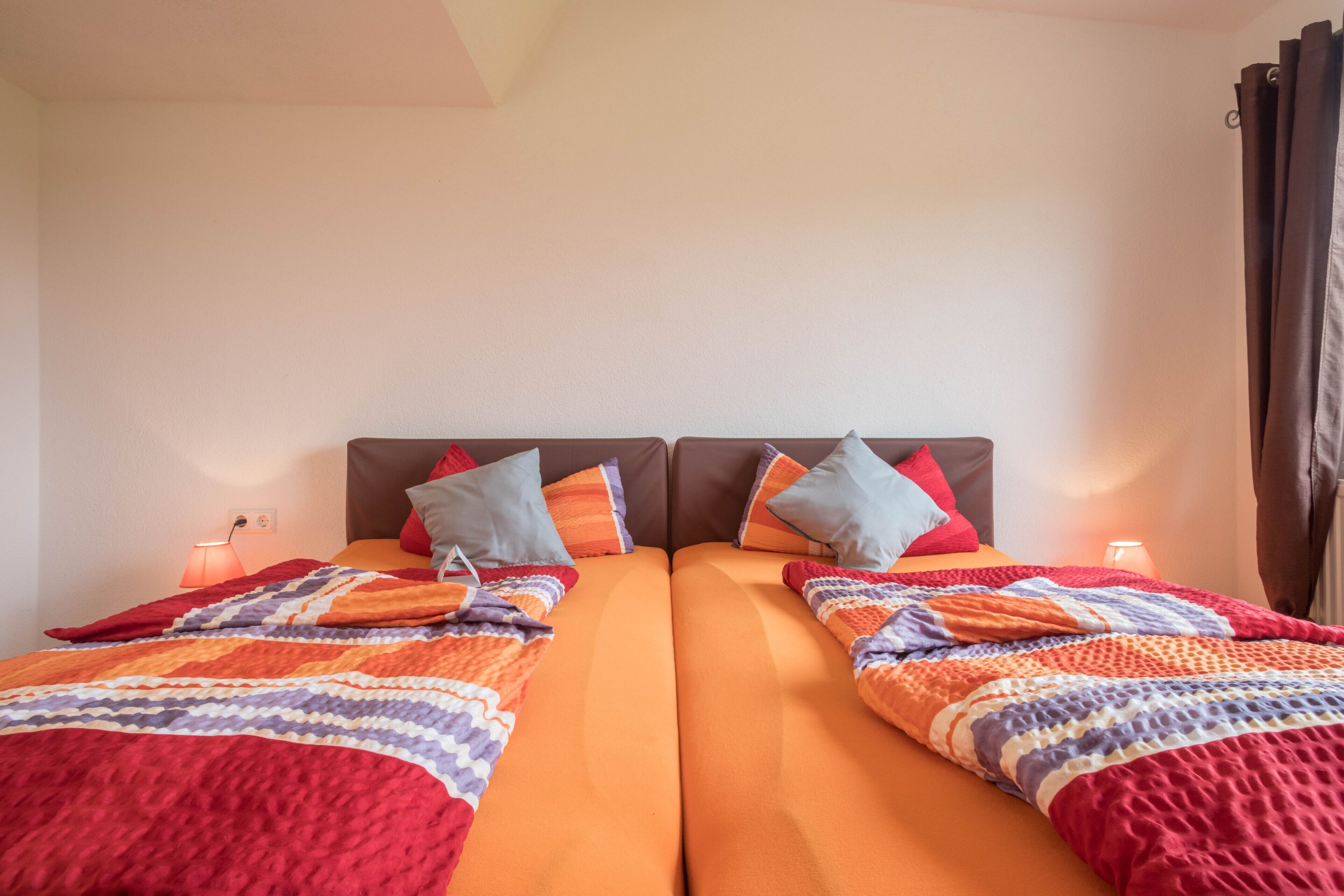 Un lit double avec une couverture à rayures, deux oreillers, une table de chevet avec une lampe et une fenêtre avec des rideaux.