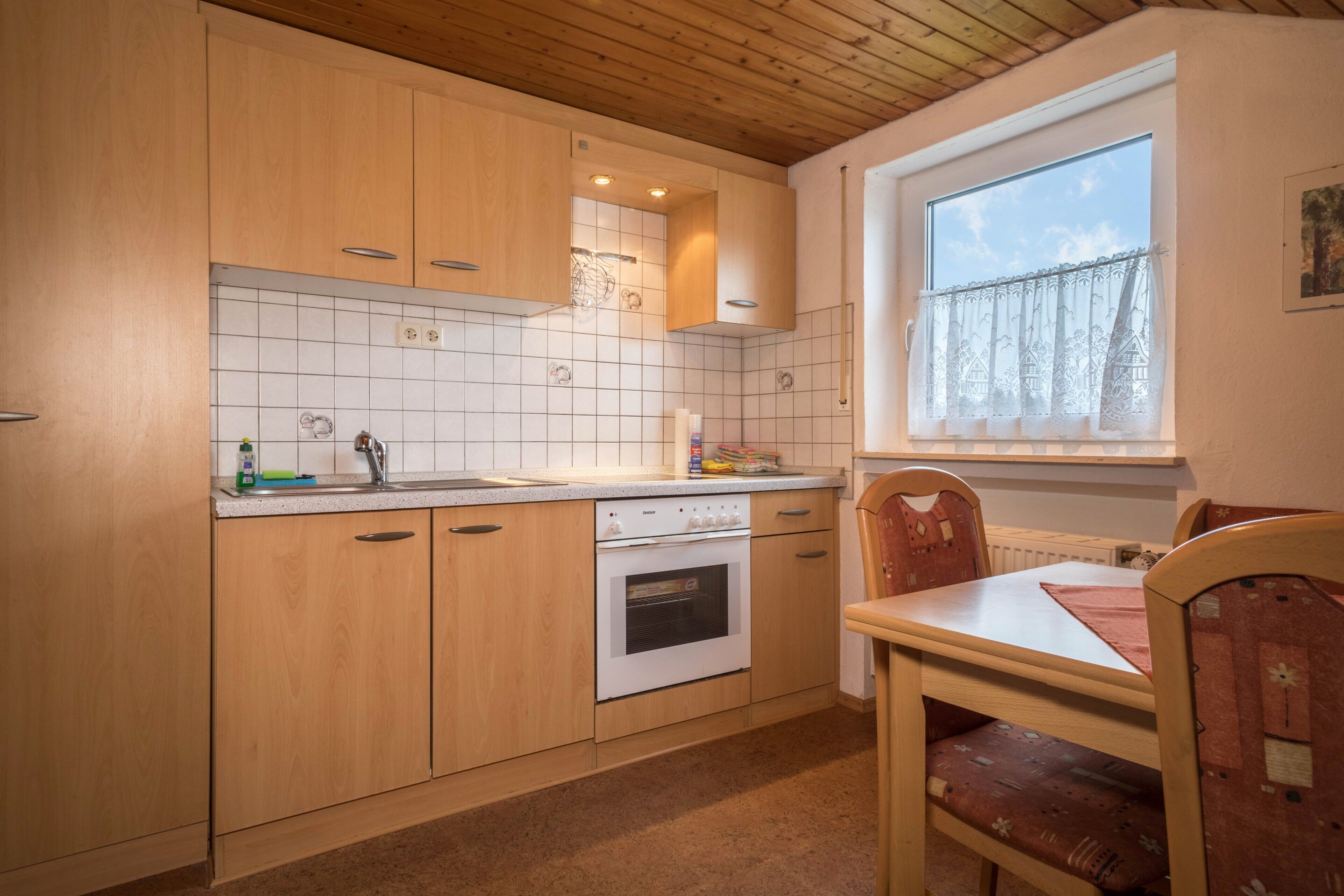 A kitchen with wooden cabinets, a tiled backsplash, a window with a curtain, and a dining table with chairs.
