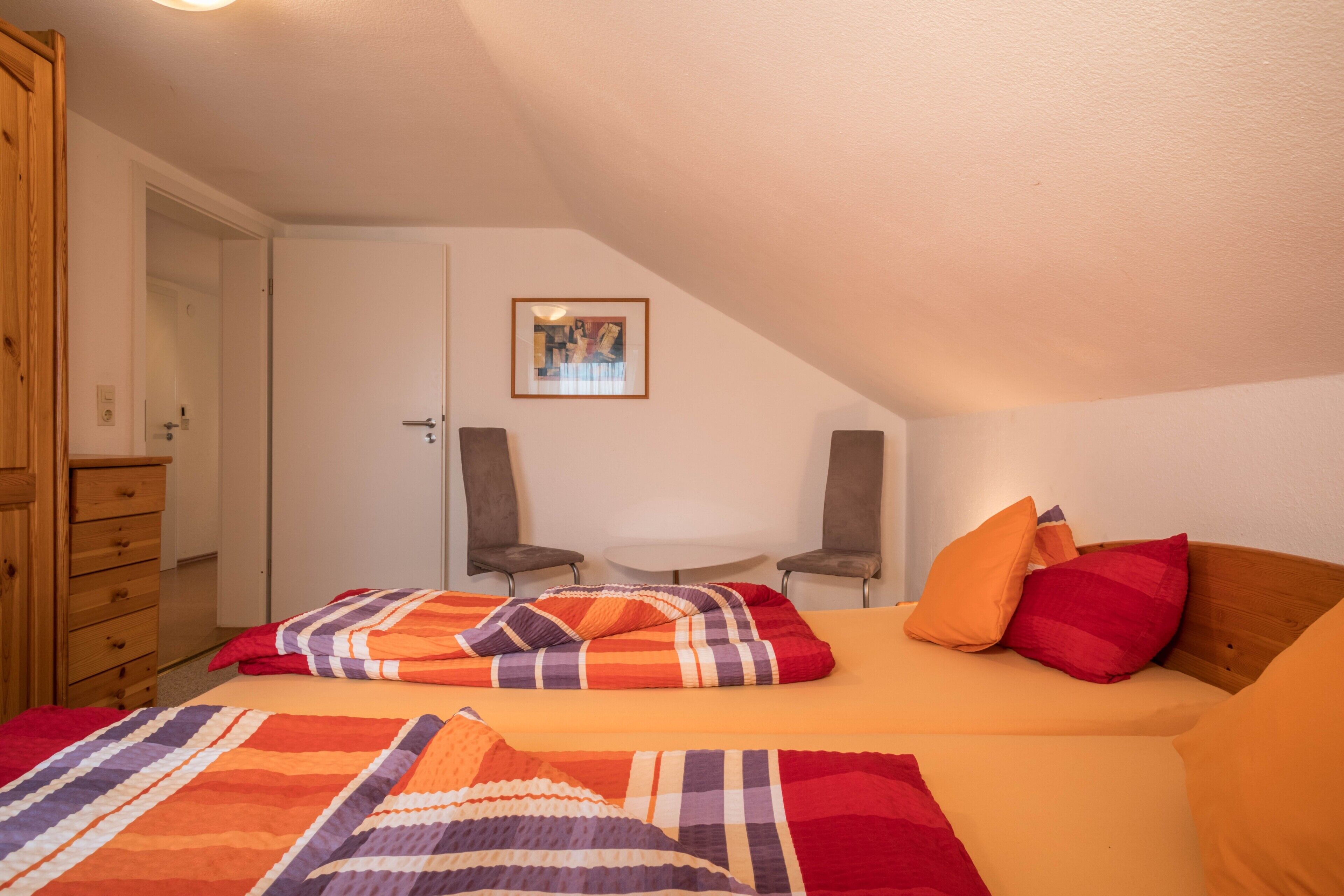 A bedroom with a bed, two chairs, a small table, and a door.