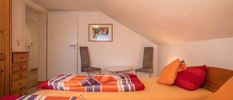 A bedroom with a bed, two chairs, a small table, and a door.