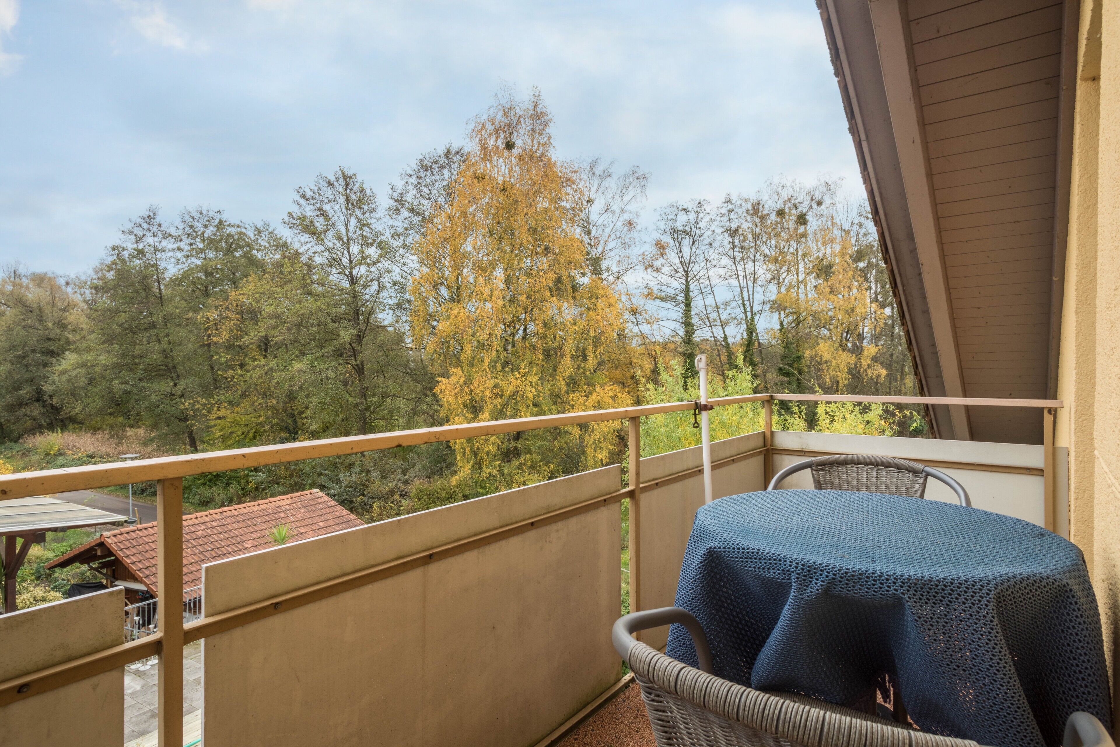 A balcony with a table and chair, overlooking a forested area with autumn foliage.