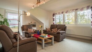 A living room with two brown sofas, a wooden coffee table, a floor lamp, and a window with a view of trees. - High-Quality Apartment “Ferienwohnung Steinhilber 1” (Eriskirch)