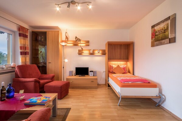 A compact room with a bed, a desk, a chair, a table, and a bookshelf.