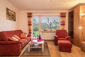 A living room with a sofa, armchair, coffee table, and a view through the window.