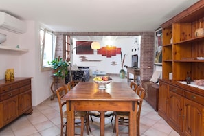 A dining area with a wooden table and chairs, a bowl of fruit, and a brick wall.