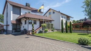 A two-story house with a tiled roof, a flag, and a well-maintained lawn.