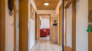 A hallway with wooden doors, a bench, a red sofa, and a green pendant light.