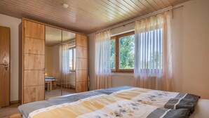 A bedroom with a bed, wooden wardrobe, and a window with curtains.