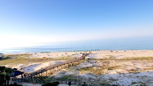 Ein Strand mit einer Holzpromenade, die zum Ufer führt, Sanddünen und Strandstühlen.