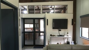 A living room with a sofa, a flat-screen TV mounted on the wall, and a sliding glass door leading to a dining area.