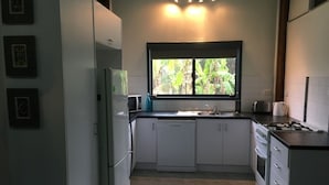 A kitchen with white cabinets, a refrigerator, a stove, and a window with a view of greenery.