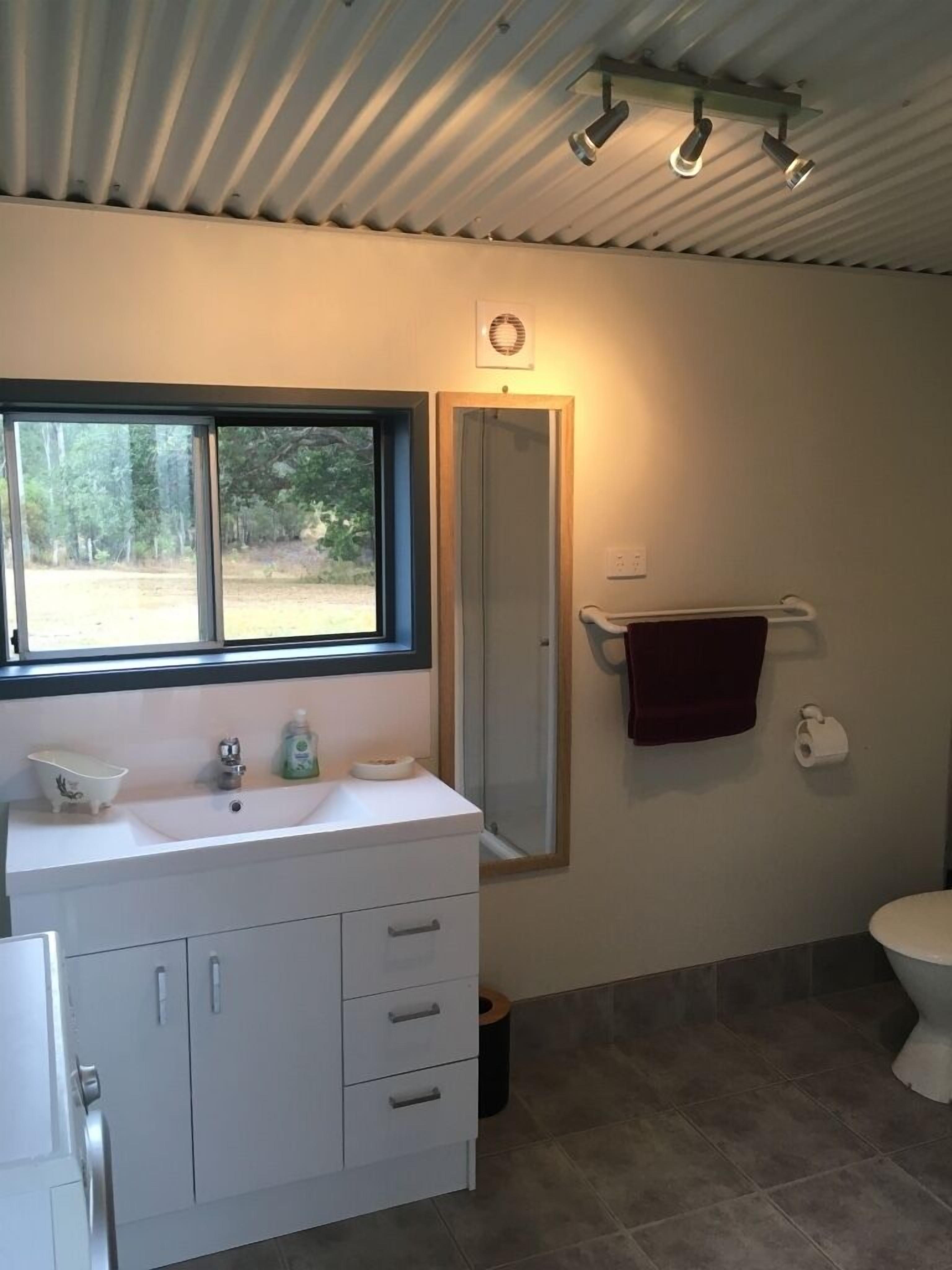 Une salle de bain avec un meuble-lavabo blanc, un miroir, une fenêtre, un porte-serviettes et des toilettes.