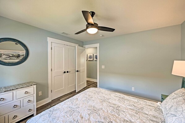 Quarto com cama, cômoda, ventoinha no teto e porta que dá para outro espaço.