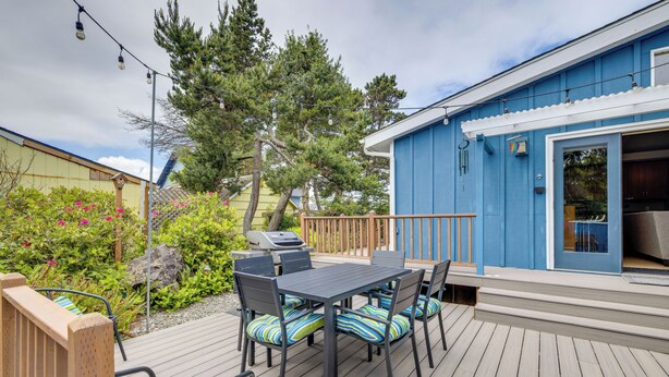 A deck with a table and chairs, a grill, and a blue building with a sliding door. - Walk to Seaside Beach! House w/ Hot Tub & Deck (Seaside)