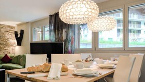 A modern dining area with a wooden table, white chairs, and a chandelier.