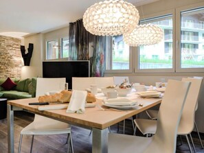A modern dining area with a wooden table, white chairs, and a chandelier.