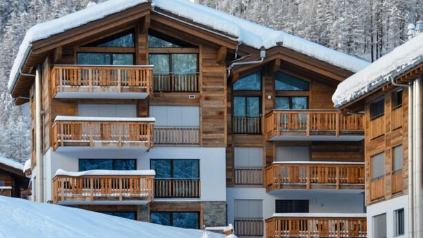 A multi-story wooden building with balconies, surrounded by snow-covered trees.