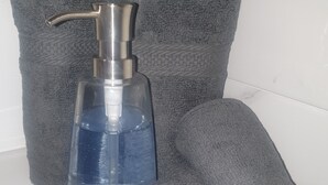 A bathroom with a white sink, a grey towel, and a blue bottle of hand soap. - Cozy Villa in Nassau with homely feel in quiet neighborhood.  (Nassau)