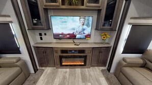 A modern living room with a flat-screen TV mounted on a wooden wall, a fireplace below, and two leather sofas.