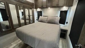 A bedroom with a large bed, wooden cabinets, and a mirror.