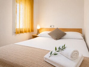 A neatly made bed with a pillow, a bedside lamp, and a rolled towel on a textured blanket.