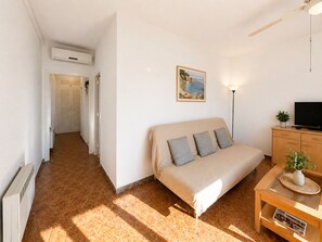 A bedroom with a bed, a TV, a lamp, a painting, and a hallway leading to a bathroom.