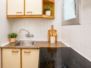 A kitchen with a granite countertop, stainless steel sink, wooden cabinets, a black stove, and a wooden cutting board with utensils.