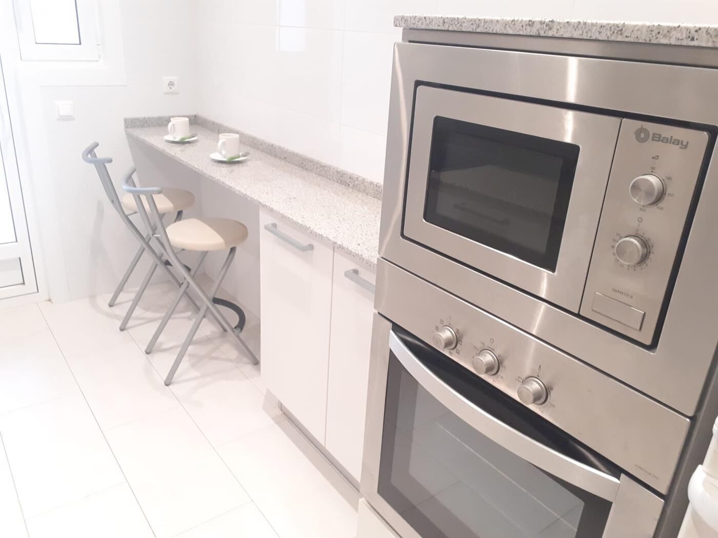 A kitchen with a built-in oven and microwave, a bar stool, and a countertop with two cups.